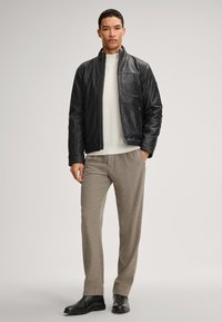 Schwarze Lederjacke mit hohem Kragen, darunter ein cremefarbener gerippter Pullover, beigefarbene Hose und schwarze Stiefel. Glatte Textur und modernes Design.
