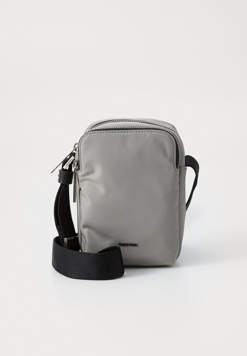 Borsa a tracolla grigia impermeabile con chiusura a zip, breve tracolla nera e un dettaglio logo discreto. Texture liscia con forma rettangolare compatta.