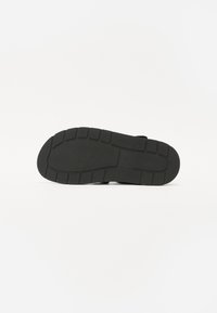 Semelle de chaussure en caoutchouc noir avec un motif de grip texturé, présentant une pointe arrondie et des rainures segmentées pour l'adhérence. Surface lisse et design durable.
