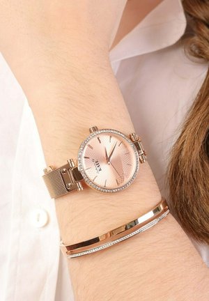 Roségoldene Armbanduhr mit einem strukturierten, hellrosa Zifferblatt und Kristallakzenten. Verfügt über ein Maschenband und ein elegantes, poliertes Armband daneben.
