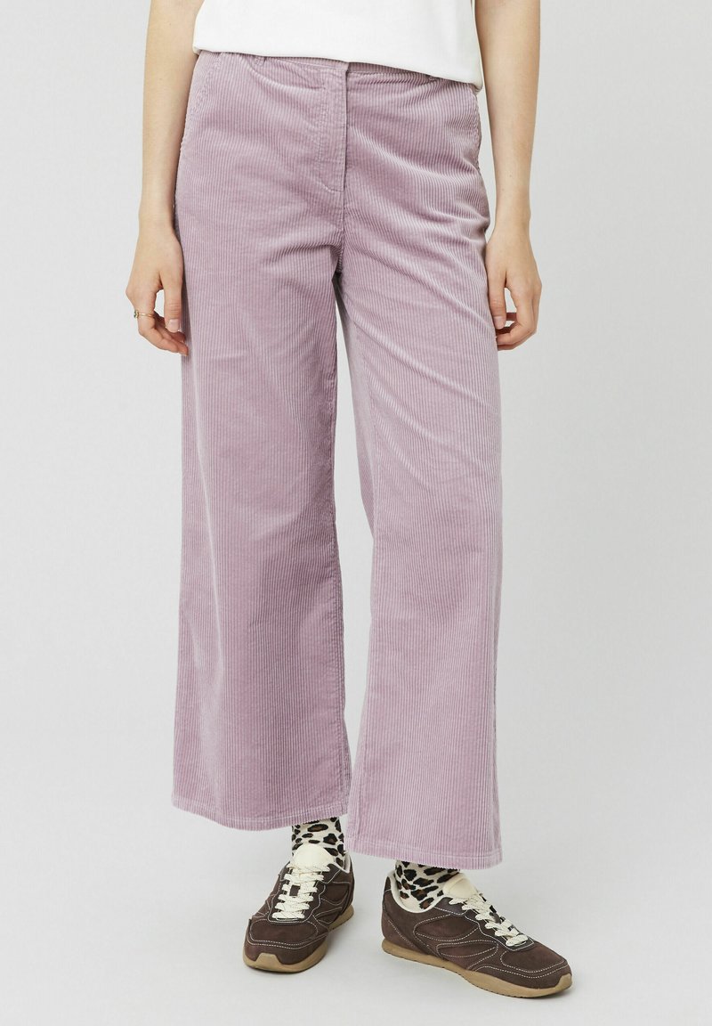 Pantalons large en velours côtelé violet clair avec des rayures verticales, dotés d'une poche avant et associés à des baskets brunes et des chaussettes à motifs.