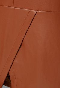 Jupe en cuir marron avec une couture diagonale et une surface subtilement texturée, mettant en avant un design contemporain et des lignes épurées.