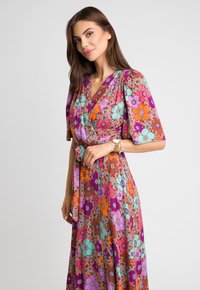 Kolorowa sukienka z kwiatowym wzorem, z krótkimi bufkami, krojem kopertowym i wiązaniem w talii. Materiał jest lekki i zwiewny.