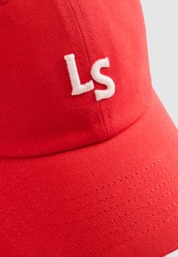 Rode baseballcap van gestructureerde stof, met op de voorkant een witte geborduurde 'LS' logo en ventilatiegaten langs de zijkanten.