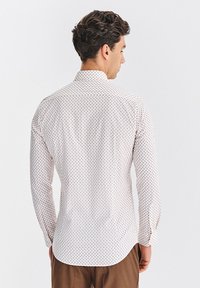 Biała koszula z długim rękawem z małymi geometrycznymi wzorami w kolorze niebieskim i pomarańczowym. Posiada wywijany kołnierz, mankiety na guziki oraz zaokrąglony dół.