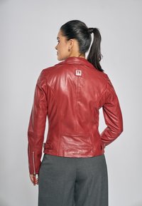 Rode leren jas met een gestructureerd design, voorzien van een klassieke kraag, mouwen met ritsen en een klein logo op de achterkant.