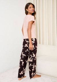 Un top scurt cu mânecă scurtă de culoare roz deschis, asociat cu pantaloni largi cu model floral negru. Țesătura pare moale și netedă, cu un design elegant.