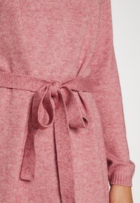 Robe en tricot rose avec une finition texturée, dotée d'une ceinture nouée à la taille et de manches longues, mettant en avant un design doux et confortable.