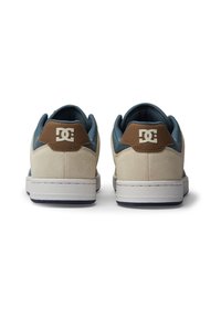 Chaussures DC avec une tige en daim beige, des accents en textile bleu et un détail en cuir marron au talon. Elles présentent une semelle en caoutchouc blanche et un logo sur le talon.