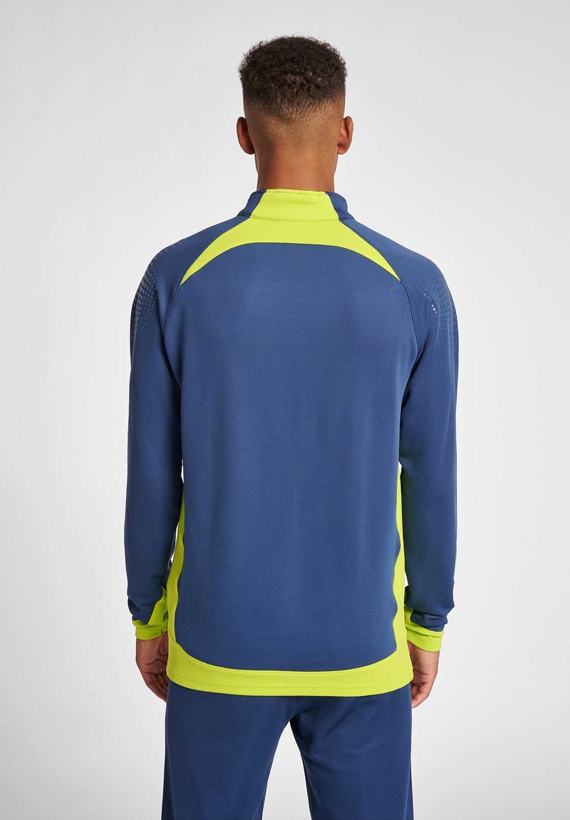 Marinblå idrottjacka med starkt gula accenter, meshpaneler och hög krage. Designad med långa ärmar och en avslappnad passform.