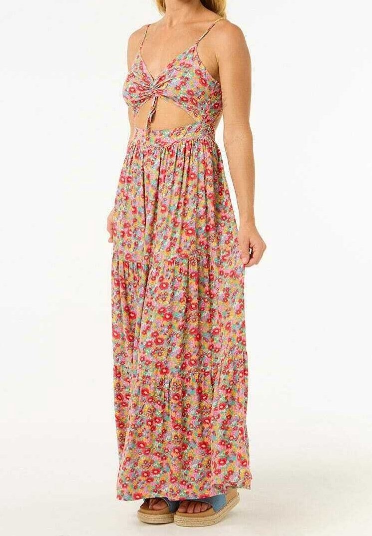 Femme portant une robe maxi fleurie sans manches avec une découpe à l'avant et un détail noué, associée à des sandales à plateforme.