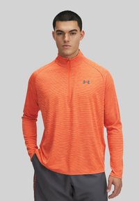 Herren-Longsleeve-Sportshirt in Orange mit Halbreißverschluss-Kragen, ausgestattet mit einem strukturierten Streifenmuster und einem kleinen grauen Logo auf der Brust.