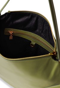 Grüne Lederhandtasche mit glatter Textur. Das Innere verfügt über ein schwarzes gemustertes Futter, eine Reißverschlusstasche mit goldfarbener Hardware und einem sandfarbenen Akzent.