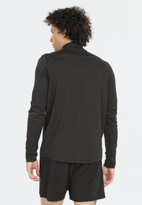 Schwarz langärmliges Sportshirt mit hohem Kragen, ausgestattet mit genähten Nähten und einer glatten Textur. Kombiniert mit passenden schwarzen Shorts.