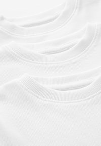 Trois t-shirts en coton blanc empilés, présentant des colliers ronds côtelés avec une texture lisse et des détails de couture réguliers.