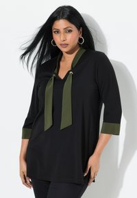 Zwarte tuniek met een V-hals en driekwartmouwen, voorzien van olijfgroene accenten en strikken bij de halslijn. Glad stofoppervlak.