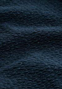 Tessuto blu scuro con una superficie ondulata, caratterizzato da piccole macchie bianche sparse, che creano un pattern di profondità e dimensione.