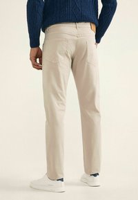 Chinos beiges avec une coupe ajustée, un design à cinq poches et des détails de couture discrets. Associés à des sneakers blanches et un pull en maille navy.