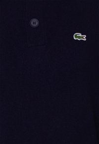 Navy polo shirt made of cotton, featuring a three-button placket and a green crocodile logo on the left chest. Soft texture, solid color.