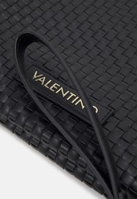 Svart vävd läderväska med en framträdande guldig "Valentino"-logotyp och ett slätt handtag i svart läder.