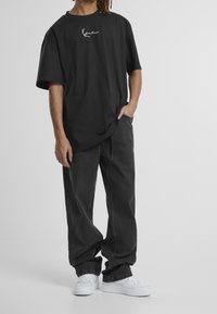 T-shirt noir surdimensionné avec un texte graphique blanc, associé à un jean gris foncé ample et des baskets blanches. Tissu en mélange de coton lisse.