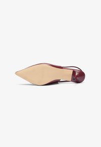Burgundin värinen nahkakenkä, jossa on korkea korko, terävä kärki ja sileä pinta; varustettu vaalealla pohjalla ja minimalistisella muotoilulla.