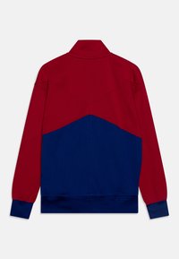 Röd och blå färgblockerat träningsjacka med hög krage, långa ärmar och ribbad fåll. Har kontrasterande texturer och sömdetaljer.