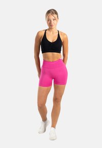 Zwarte, strakke sportbeha met een geplooid voorpand, gecombineerd met hoogwaardige roze shorts. De outfit heeft een gladde, elastische textuur.