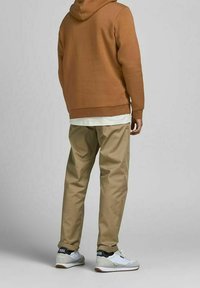 Felpa cappuccio marrone, camicia bianca a strati, pantaloni chiari in khaki e sneaker bianche con accenti neri. Tessuto morbido e vestibilità rilassata.