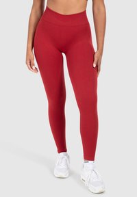 Leggings rossi a vita alta realizzati in tessuto elasticizzato, con una texture liscia e un design aderente, abbinati a scarpe da ginnastica bianche.