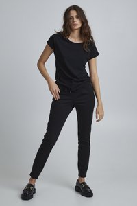 Schwarzes Baumwoll-T-Shirt mit umkrempelten Ärmeln, kombiniert mit schwarzen Jogginghosen mit elastischem Bund. Schwarze Plateauslippers runden das Outfit ab.