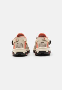 Sandales de plein air beiges avec des accents orange. Panneaux en maille, strap ajustable et semelle texturée. Conception robuste avec un motif de semelle prononcé.