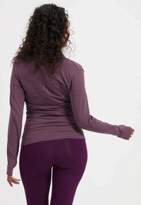 Langarmshirt in Lila, aus weichem Stoff und mit figurbetontem Design. Verfügt über abgerundete Nähte und einen runden Ausschnitt, kombiniert mit dunkelvioletten Leggings.