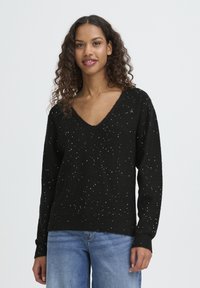 Black knitted sweater with a V-neck, featuring scattered white specks. Long sleeves and a relaxed fit, made from soft, textured fabric.