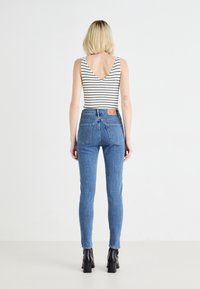 Jeans de mezclilla azul de tiro alto con una silueta ajustada, que presentan bolsillos cosidos y un parche de cuero en la parte trasera, combinados con una camiseta de tirantes a rayas.