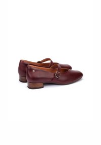 Bailarinas de cuero burdeos con puntera afilada, tira para el tobillo y pequeño tacón de madera. Presentan hebilla metálica y textura suave.