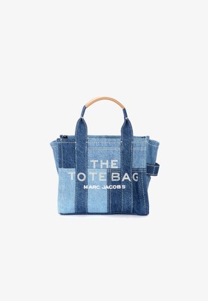 Denim patchwork tote bag with tan handle featuring white text "THE TOTE BAG MARC JACOBS" on front center.