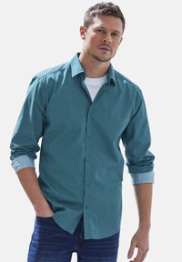 Türkisfarbenes Hemd mit Musterdesign und kontrastierenden hellblauen Manschetten, kombiniert mit dunkelblauen Jeans. Lässige Passform und aus Baumwolle.