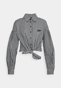 Chemise à carreaux vichy noir et blanc avec de longues manches bouffantes et un détail en nœud à l'avant, comportant des boutons noirs et une broderie de logo.