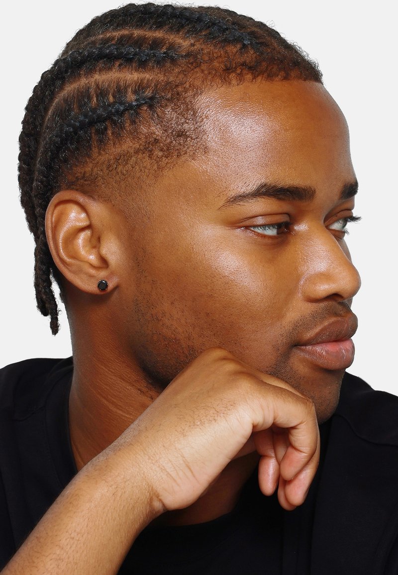 Profil d'une personne avec des cheveux tressés, une peau foncée et une texture lisse, portant une chemise noire et une boucle d'oreille noire.