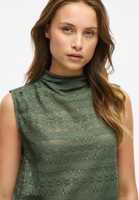 Groene kanten top met een hoge halslijn, mouwloos ontwerp en intricatge bloemenpatronen, met een licht doorzichtige textuur.