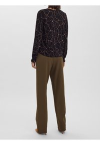 Haut noir à manches longues avec un motif abstrait beige, associé à un pantalon large vert olive. Le haut présente des poignets froncés et un col rond.