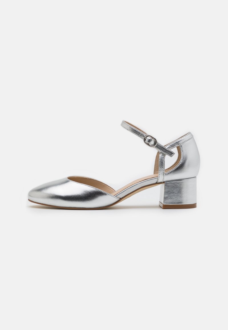 Chaussure Mary Jane en métal argenté avec un bout arrondi, une sangle au niveau de la cheville et un talon bloc. Texture lisse avec une finition brillante.