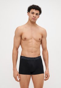 Boxer-briefs noirs avec une texture douce, présentant une ceinture sombre contrastante arborant le texte "ARMOUR" dans une police subtile. Fabriqués en matériau extensible.