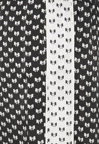 Tissu en noir et blanc avec un motif de nœuds répétés, une bande blanche contrastante, une surface texturée et un design graphique audacieux.