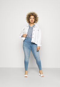 White denim jacket over a blue striped blouse, paired with light blue skinny jeans and white heeled sandals. Smooth textures and casual style.
