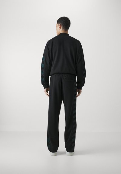 Black track suit featuring a zip-up jacket with a high neckline and patterned side stripes, paired with matching elasticated waist pants.