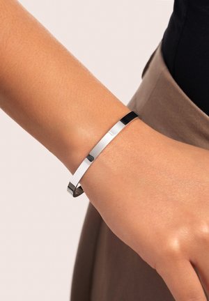 Pulsera de brazalete de metal plateado con un acabado suave y pulido. Curvatura sutil, diseño minimalista y extremos abiertos para un ajuste ajustable.