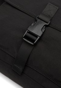 Borsa di stoffa nera con una fibbia in plastica resistente e una tracolla intrecciata, con cuciture visibili e una superficie liscia.