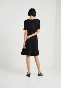 Abito nero con maniche corte, zip sul retro e gonna svasata con intagli circolari lungo l'orlo. Tessuto liscio, design fino al ginocchio.